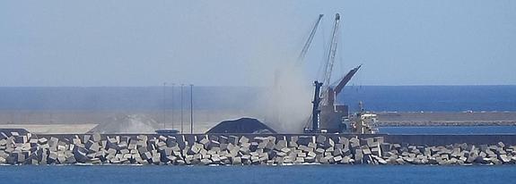 La nube de polvo levantada por las labores de carga y descarga apenas deja ver las grúas y los dos barcos atracados en la ampliación del puerto de El Musel. 