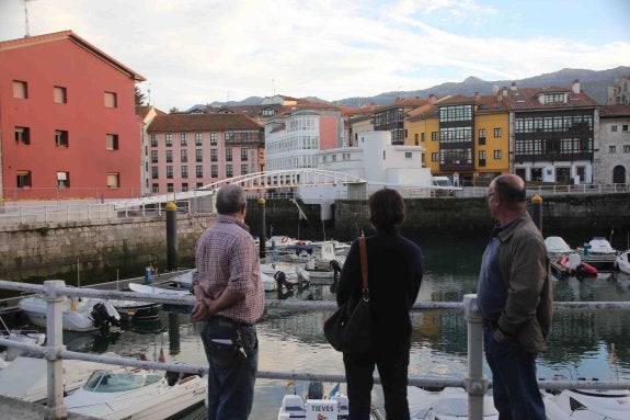 Varios vecinos observan la pasarela peatonal instalada en le puerto de Llanes y que no se abrirá al público hasta dentro de un mes. 