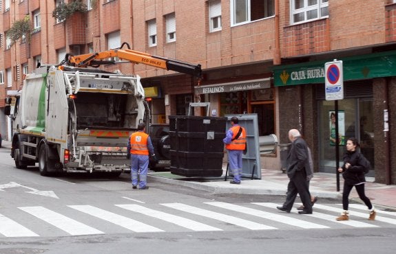Operarios realizan la recogida de basura en un contenedor de La Pola. 