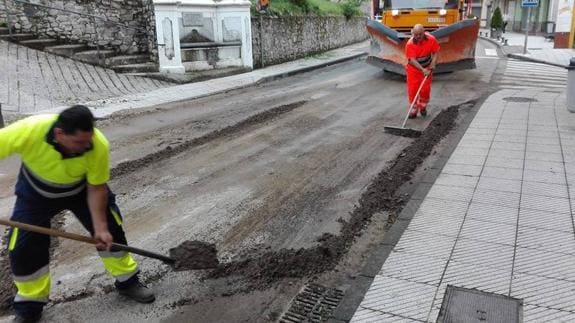 Operarios municipales limpian en Pola de Allande la mezcla de granizo y basura que se acumuló en la vía.