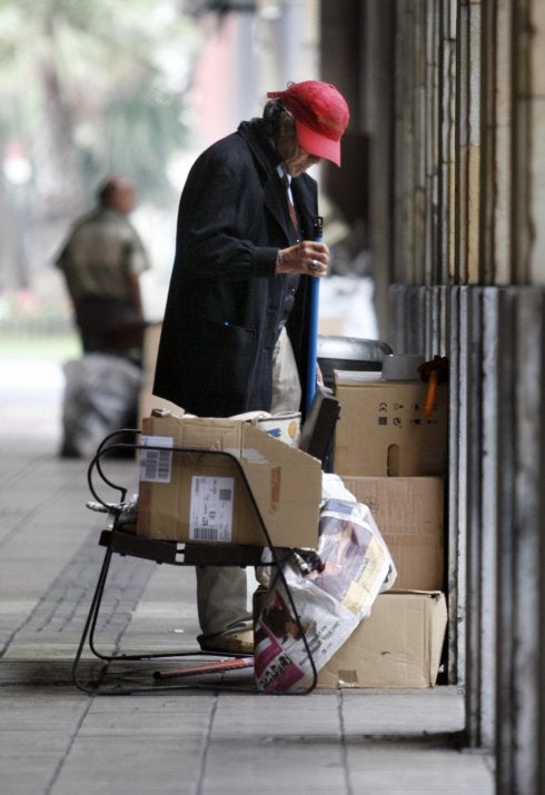 Un 'sin techo' camina entre cartones. 