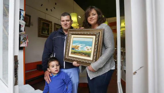 Los hermanos Ana y Fernando Martín, con el hijo de él, Daniel, posan junto al cuadro de su madre 'La playa del Silencio'