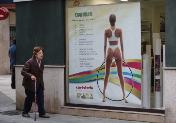 Una señora pasa por delante del cartel de Cubiella Informática en el barrio de El Carmen, que el Principado considera sexista. 