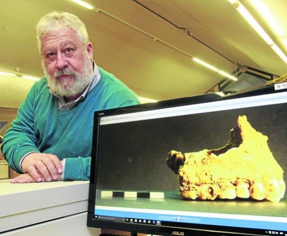 Marco de la Rasilla, en su despacho del campus de El Milán, con una fotografía de la mandíbula con restos de corteza de álamo de uno de los 13 de El Sidrón. 