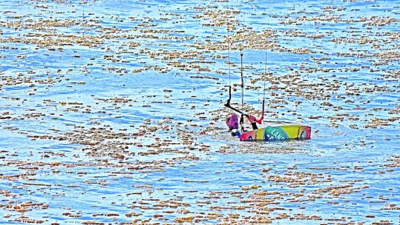 Un practicante de kite-surf intenta abrirse paso entre las manchas en la playa de Salinas