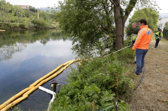 Varios operarios de Inteco Astur controlan las barreras de absorción colocadas en el Deva, a su paso por Unquera, y las mueven hacia las orillas. 