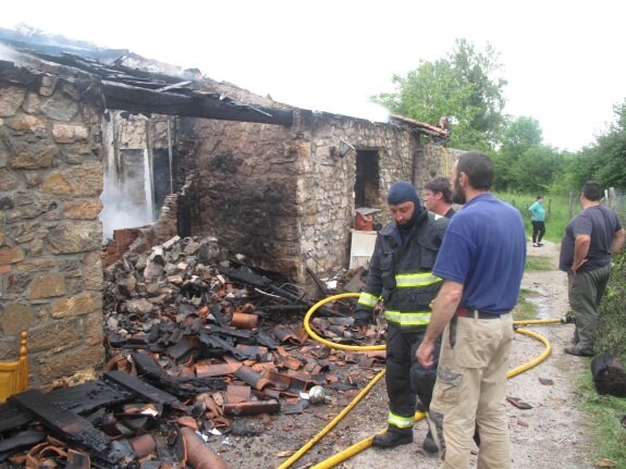 Los vecinos y varios bomberos, frente a la vivienda derruida tras controlar el incendio. 