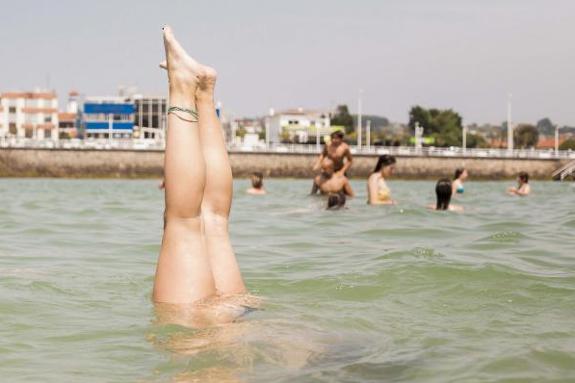Una joven hace el pino dentro del agua en la playa de San Lorenzo de Gijón 
