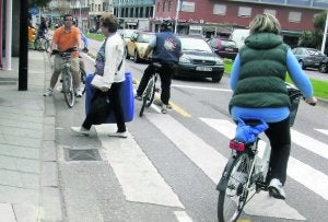 Varios ciclistas esperan a que una mujer cruce la calle con los coches detenidos en el semáforo. ::
CITOULA