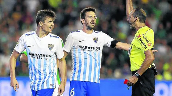 Ignacio Camacho, a la derecha, conversa con el árbitro, que muestra una amarilla a Diego Llorente.