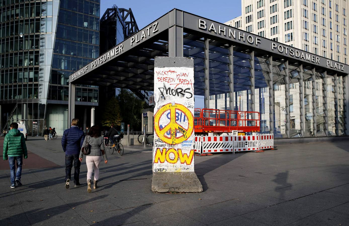 Transeúntes caminan junto a un tramo del Muro de Berlín, en la plaza Potsdamer Platz de Berlín.