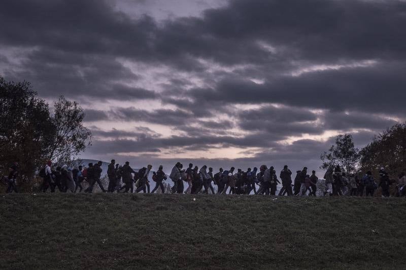 Un grupo de migrantes camina encima de un dique mientras la policía antidisturbios eslovena los acompaña al campo de registro de Dobova (Eslovenia). Serie ganadora de Noticias de Actualidad.