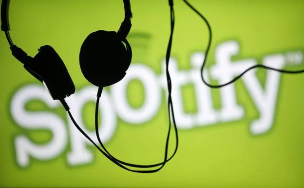 Unos auriculares delante del logotipo de Spotify. 