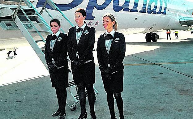 Tres azafatas forman junto a su avión a pie de pista.