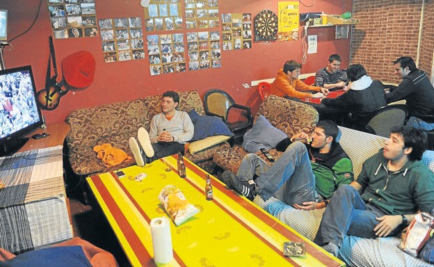 Varios jóvenes se divierten viendo la tele y jugando a las cartas en una lonja de Vitoria.