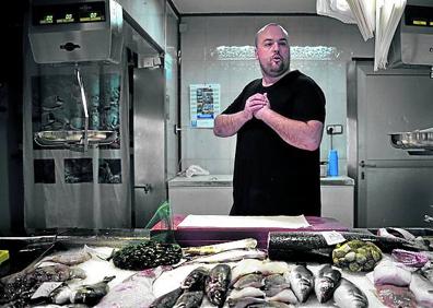 Imagen secundaria 1 - Carmen Jiménez, con su familia, asomada a la ventana por donde intentaron robarle. El pescadero Sergio López analiza la situación en su puesto del mercado. Julián Jiménez explica lo ocurrido el miércoles en su sede.