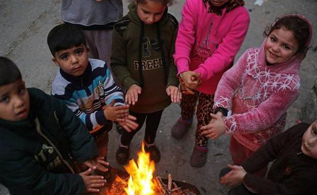 Un grupo de niños refugiados se calienta con el fuego.