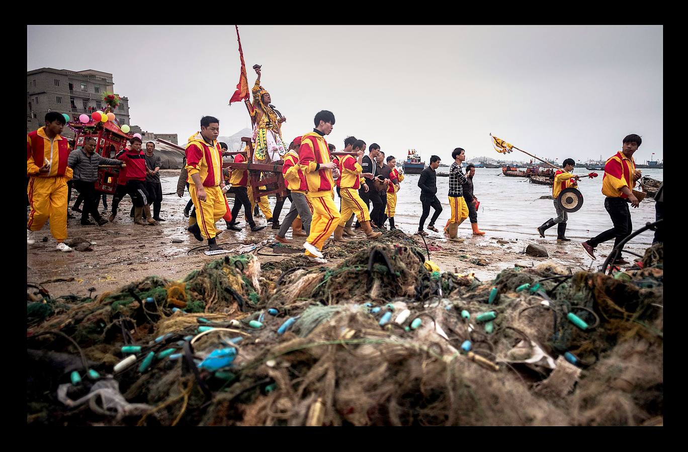 «El tablero de los dioses oceánicos» es uno de los más sorprendentes festivales que se celebran en Fuye, una localidad de la isla de Nanri, en la provincia china de Fujian. Vestidos con prendas bordadas y coronadas sus cabezas con intrincadas coberturas, una veintena de participantes cantan y blanden espadas y estandartes mientras son transportados hacia el mar en palanquines portados por convecinos. La pesca sigue siendo un trabajo arriesgado para los moradores de Fuye, que se hacen a la mar en pequeñas embarcaciones acompañados por imágenes y estatuillas para que los dioses les protejan. «Podemos pedirles que nos mantengan a salvo en el mar, pero no pueden darnos peces ni decirnos dónde hay más,» dijo Zhou, uno de tantos pescadores que estudia inglés con la esperanza de obtener trabajo en un barco de altura.