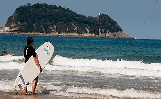 El ratón de Getaria se perfila ante un surfista presto a coger olas en la playa de Zarautz.