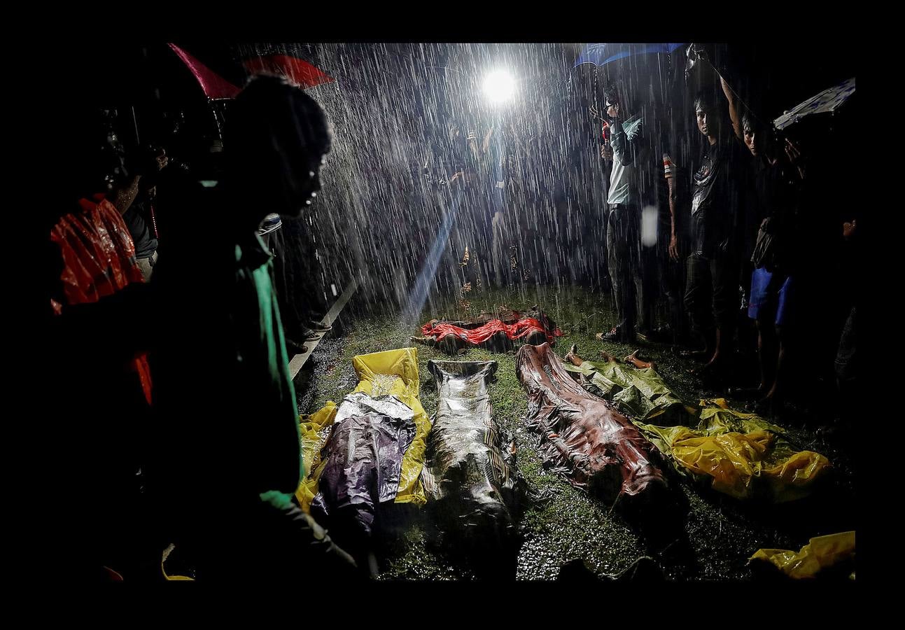 Un grupo de personas se reúnen bajo la lluvia alrededor de los cuerpos sin vida de unos refugiados rohinyás tras morir ahogados en la playa de Inani, cerca de Cox's Bazar (Bangladés), el 28 de septiembre de 2017.