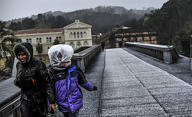 Dos peatones desafían las inclemencias meteorológicas en la pasarela Arrupe.
