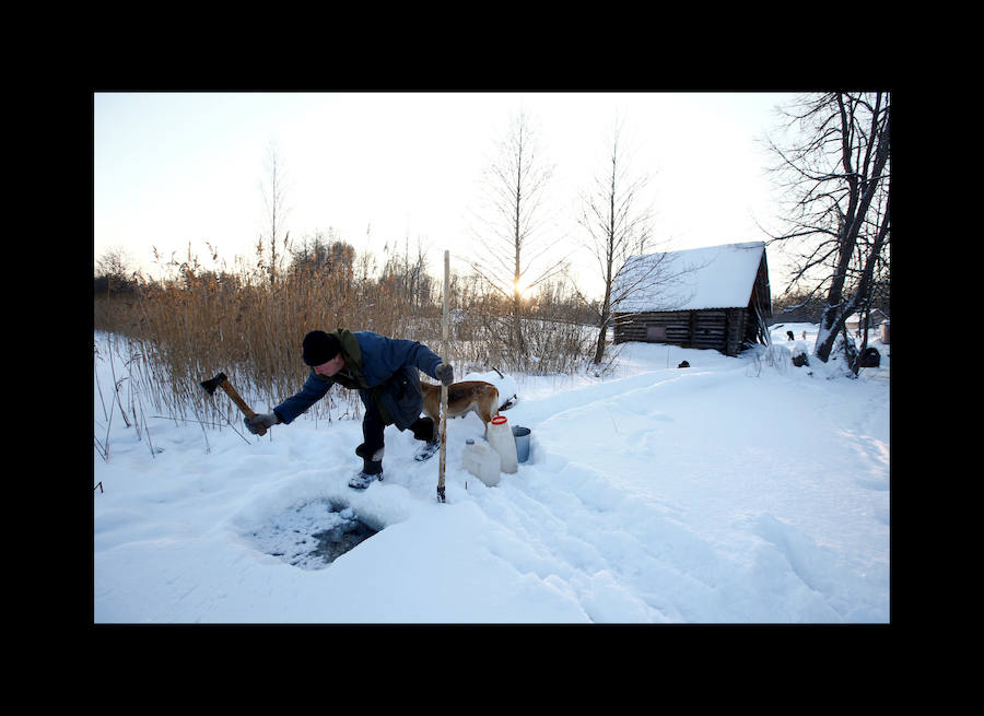Yuri Baikov, de 69 años, hace un agujero para extraer agua del río congelado en su pequeña granja situada en un bosque cerca de la aldea de Yukhovichi, Bielorrusia, el 7 de febrero de 2018. Yuri y su esposa han vivido durante más de un cuarto de siglo en una choza primitiva en un bosque. Solían vivir en Yukhovichi, la aldea más cercana, como agricultores, criando vacas y aves de corral. Pero vivir cerca de otras personas no les sentaba bien. «No podemos dejar a nuestros animales y pájaros ni siquiera por un día, y no queremos»