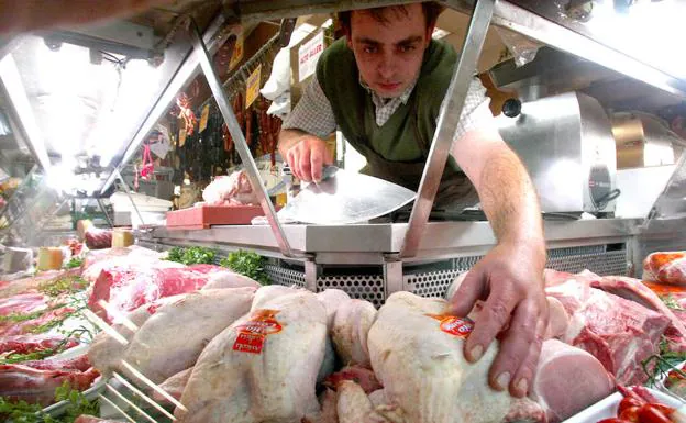 Un carnicero coloca pollos en el expositor de su local.