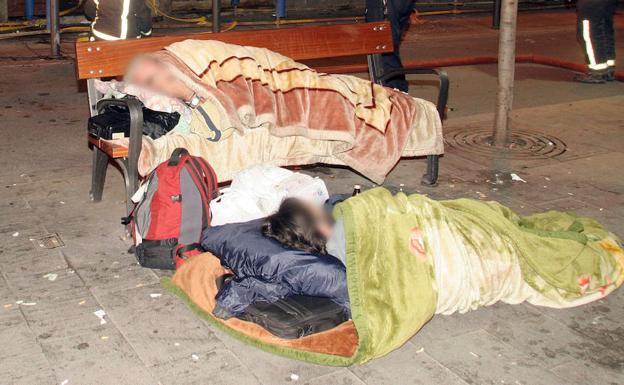 Dos hombres duermen en la calle arropados con mantas.