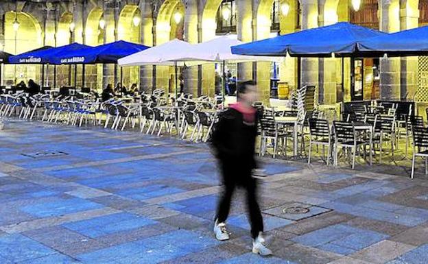 Un joven pasa frente a una hilera de terrazas colocada en uno de los laterales de la Plaza Nueva de Bilbao.