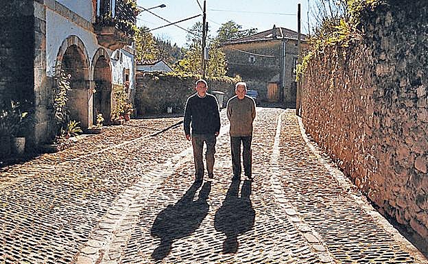 Dos vecinos caminan por una calle empedrada.