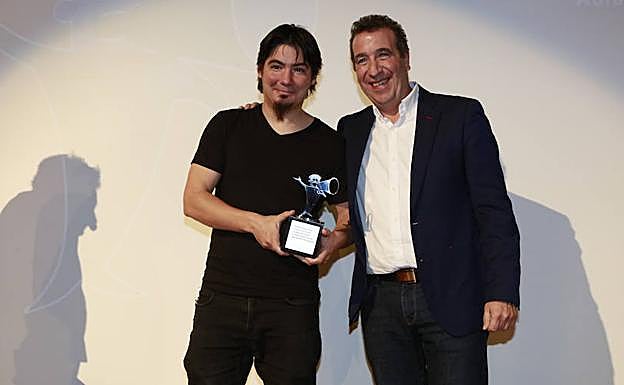El director Paul Urquijo recibe el galardón al mejor largometraje de manos de Jon Urresti, presidente de la Fundación Vital. A la izquierda, un fotograma de la película.