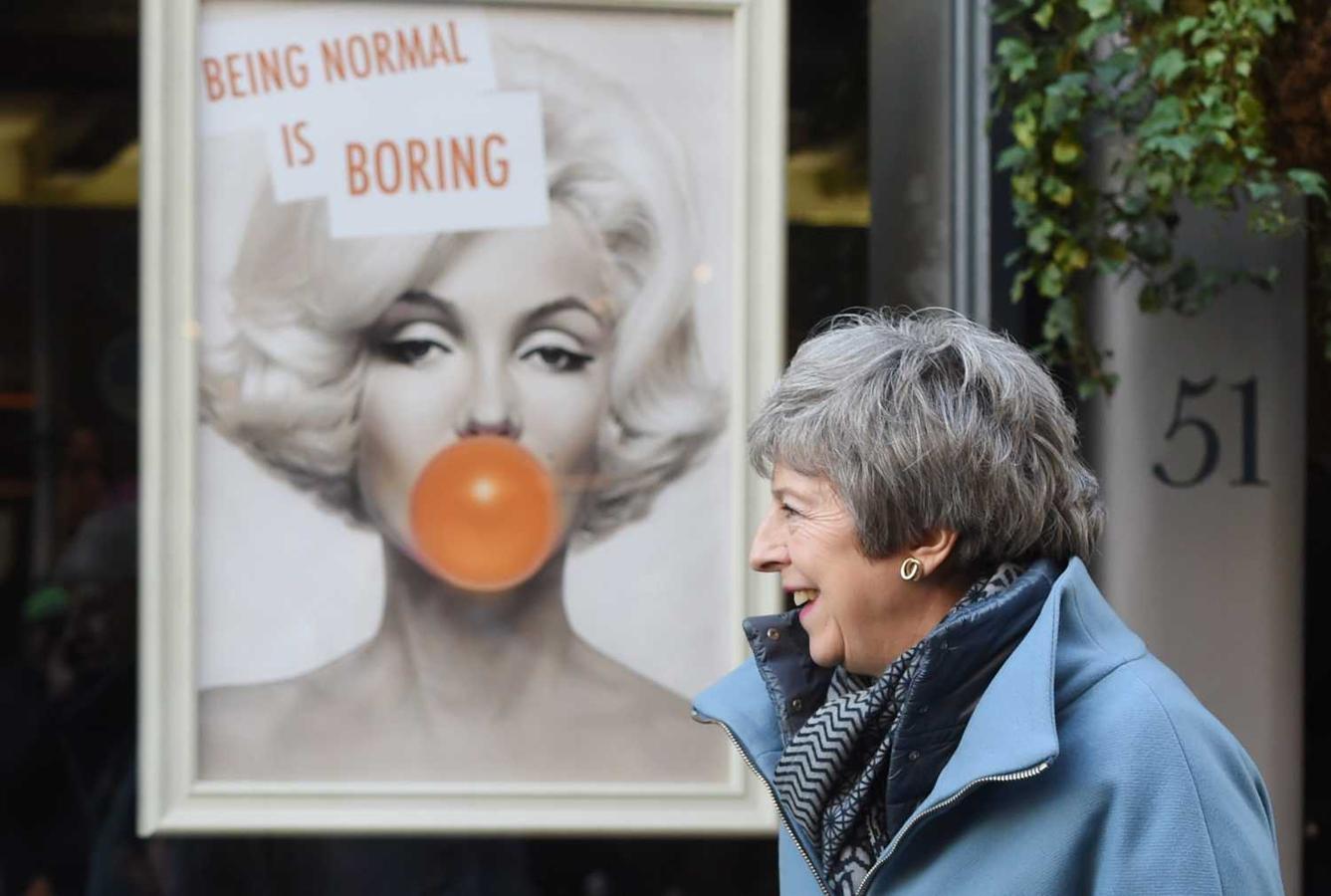 La primera ministra británica, Theresa May (c), sonríe tras visitar una peluquería durante su visita a Salisbury (Reino Unido). Al fondo un cartel publicitario con la cara de Marilyn Monroe y el lema “Ser normal es aburrido “
