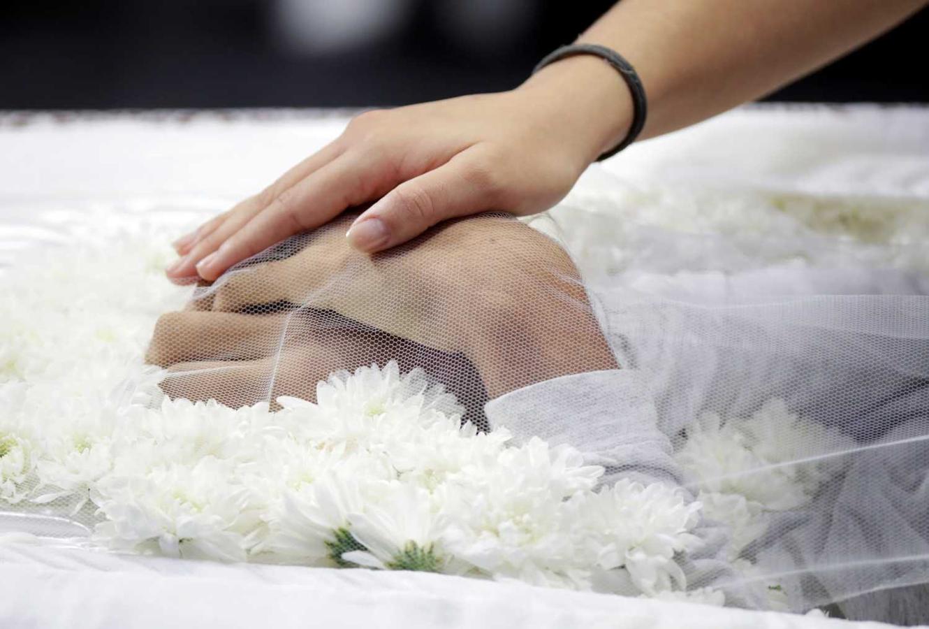 Una persona tocando las manos de una de las victimas de la masacre de la Escuela Estadual profesor Raul Brasil, durante el funeral celebrado en Suzano, Brasil 