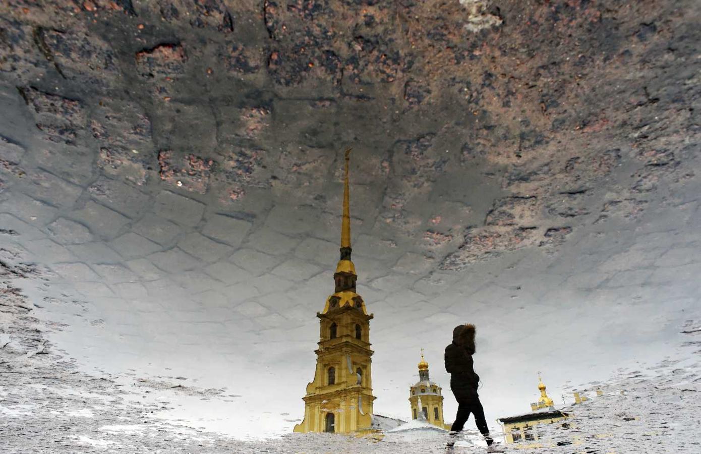 La silueta de una mujer se refleja en un charco, mientras pasa frente a la Catedral de San Pedro y San Pablo, en San Petersburgo, Rusia 