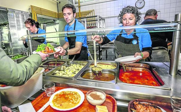 Tres de los voluntarios sirven alubias, merluza y arroz con leche a los usuarios del comedor social. 