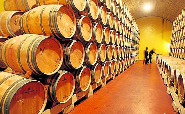 Dos operarios trabajan en una nave de barricas de una bodega. 