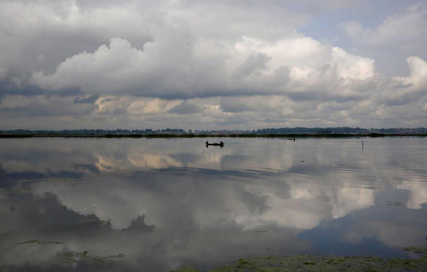 Un hombre navega en barca por el lago Dal mientras las nubes se reflejan en el agua, en Srinagar, la capital estival de la Cachemira india. 