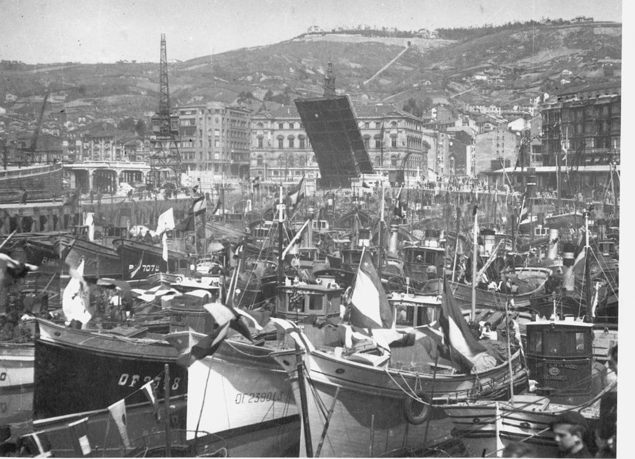 Embarcaciones pesqueras con banderas españolas amarradas junto al muelle del Arenal. Al fondo el puente del Ayuntamiento derribado con una de sus partes abierta