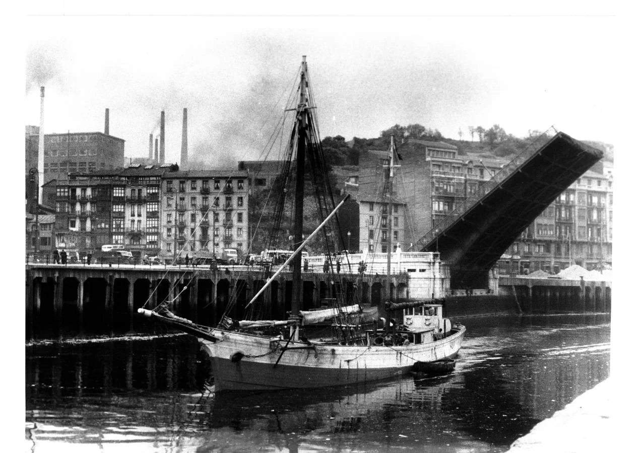 Carbonero pasando bajo el puente del Ayuntamiento, Bilbao, al fondo las chimeneas de la fabrica de Etxebarria, hacia 1957