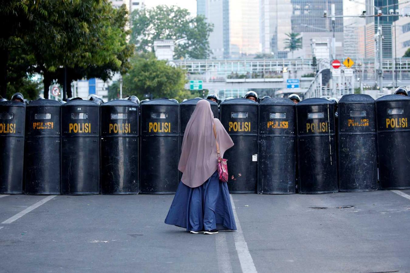 Una mujer frente a una barrera formada por policías antidisturbios de Indonesia tras el anuncio de los resultados de las elecciones presidenciales