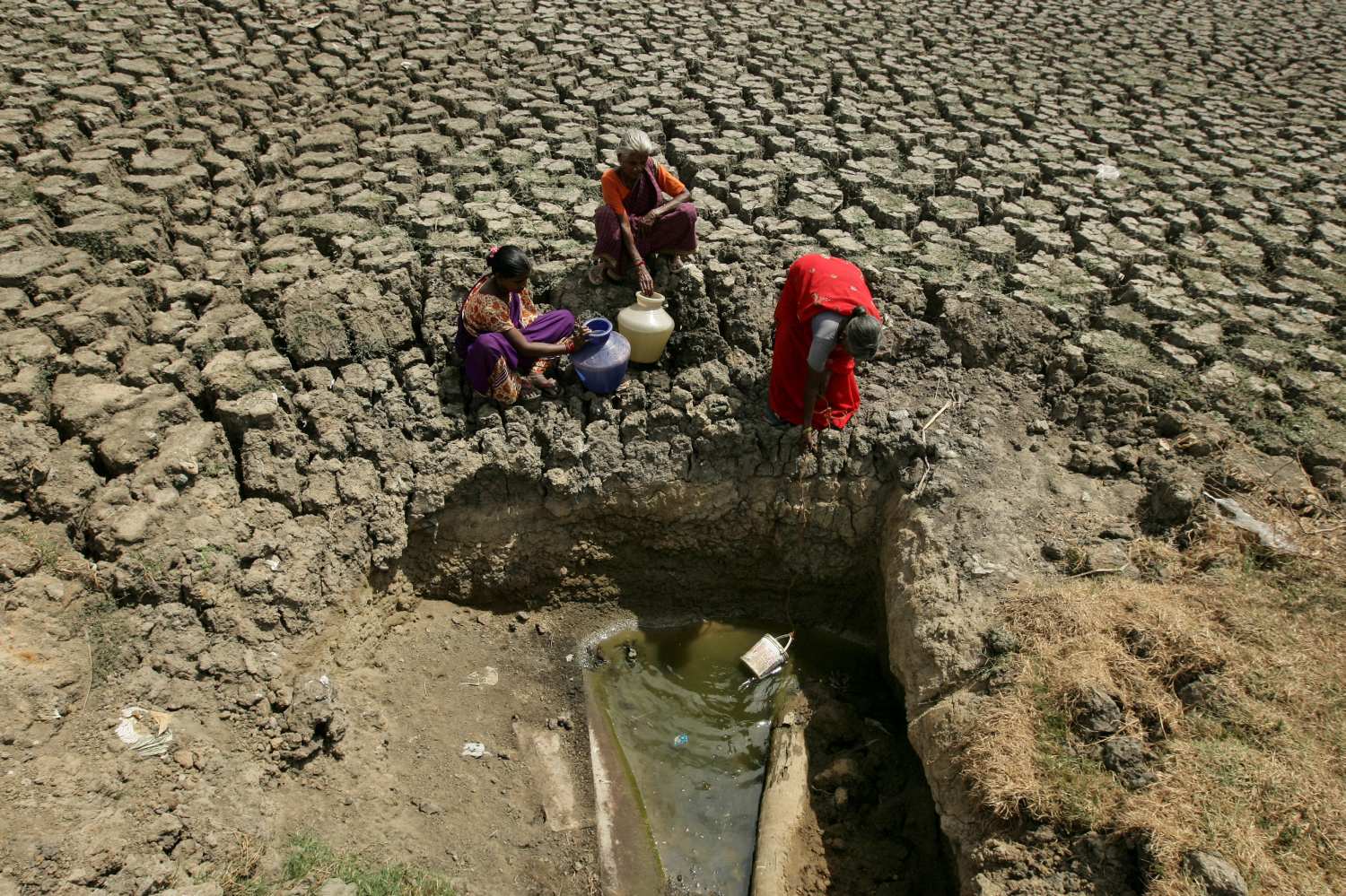 Mujeres recogen agua de una abertura hecha por residentes en un lago seco en Chennai, India.