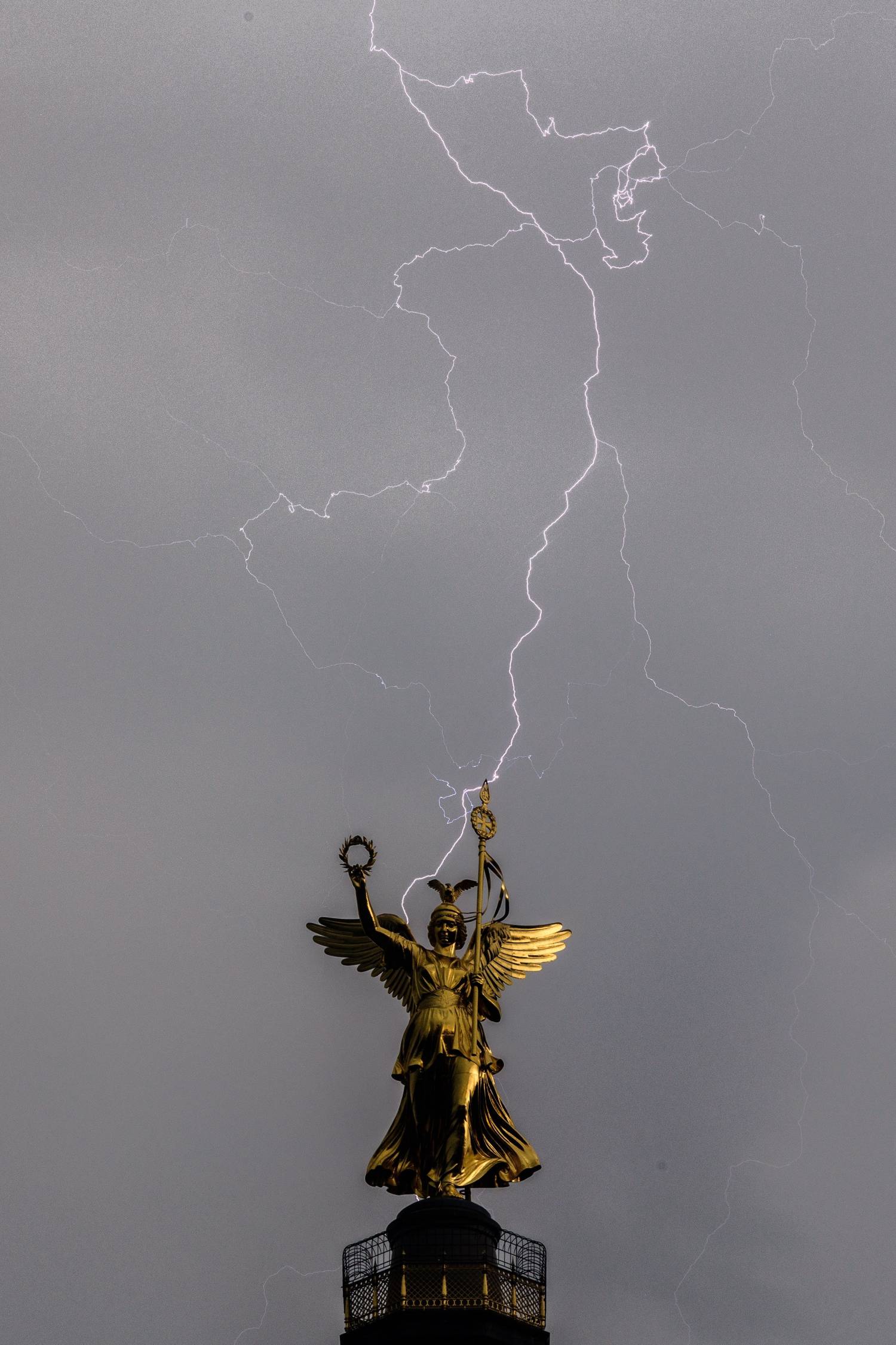 Un rayo cae tras la estatua que corona la Columna de la Victoria en Berlín (Alemania), durante una tormenta eléctrica sobre el cielo de la capital germana. 