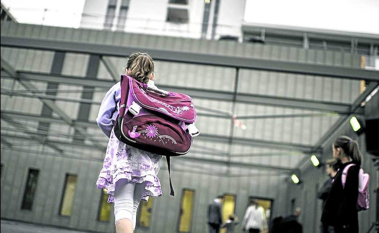 Una niña atraviesa el patio cargada con la mochila camino de clase.