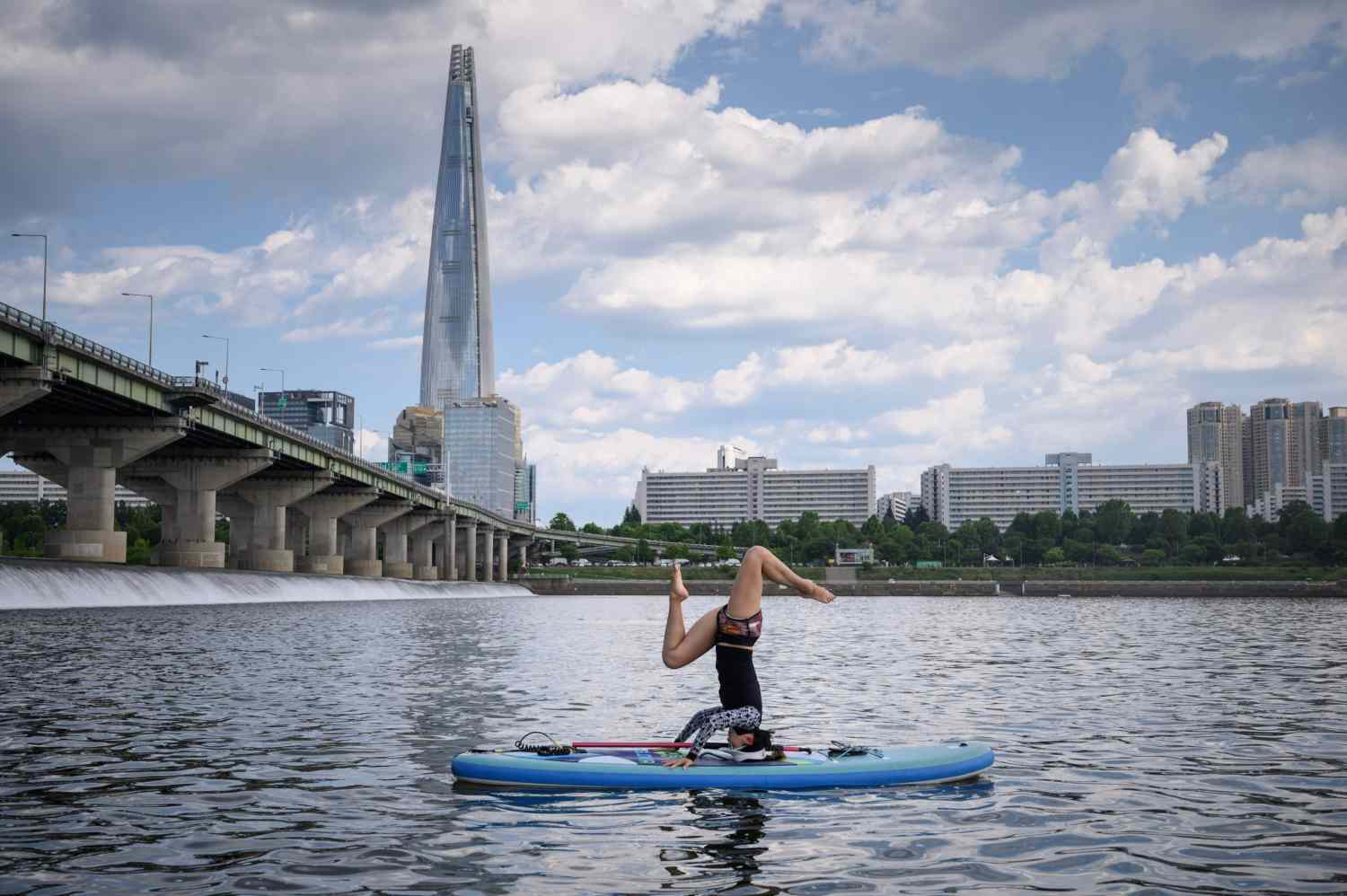 Una mujer realizando una postura de yoga en una tabla de paddle frente a la Lotte Tower, en el río Han, Seúl.