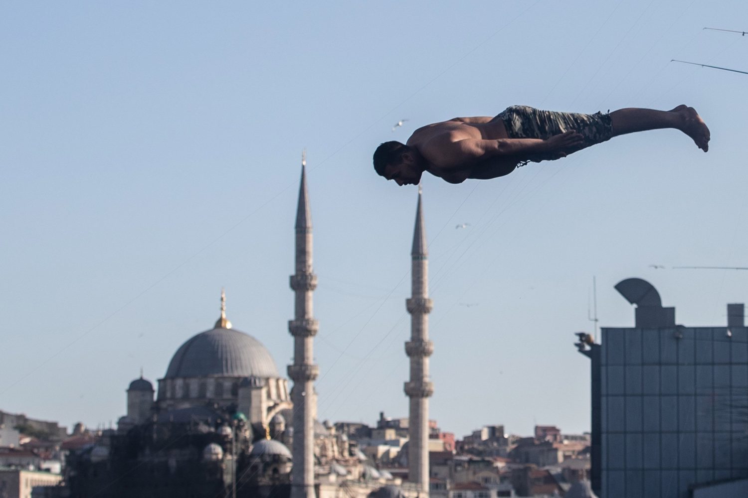 Un hombre se lanza al agua desde el puente Galata con la Mezquita Nueva de fondo en Estambul (Turquía). 