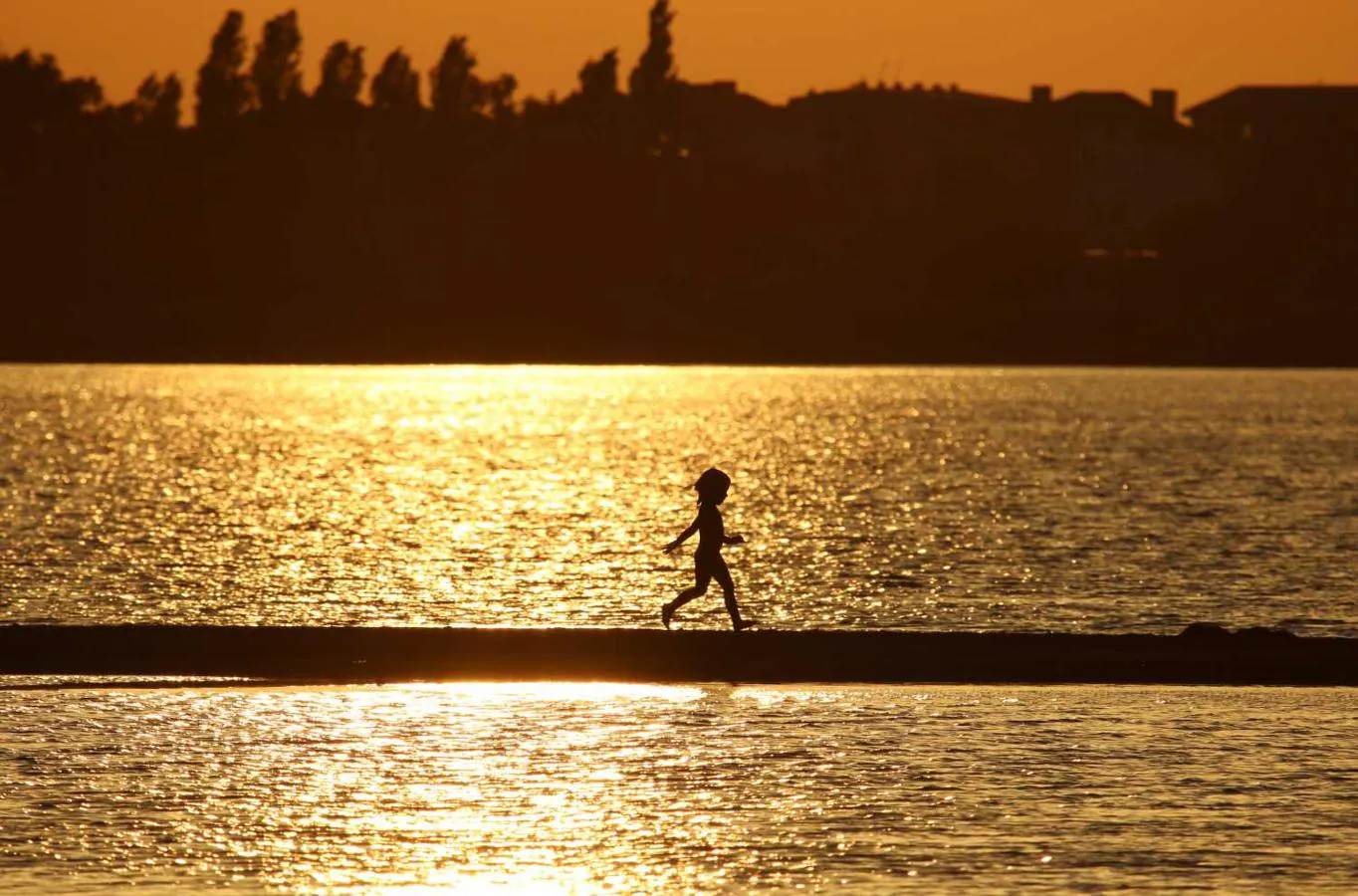 Un niño corre a lo largo de un banco de arena en medio de las aguas del lago Moynaki durante la puesta de sol en Yevpatoriya, Crimea