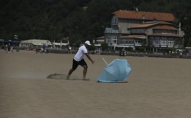 Un bañista persigue una sobrilla en la playa de Ereaga.