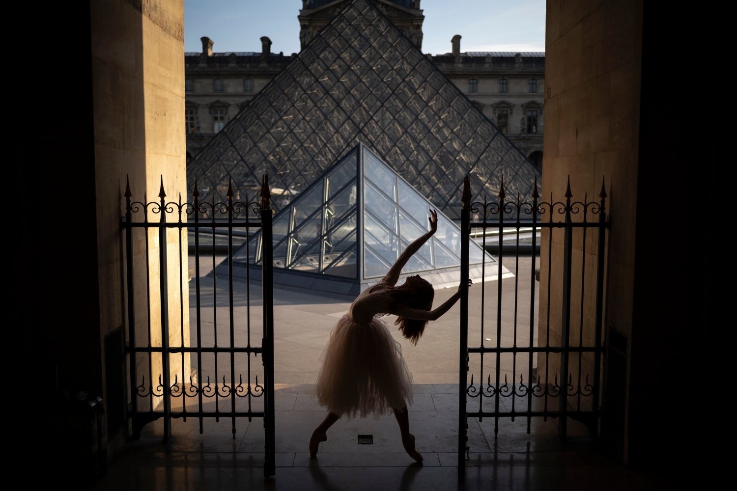 Una bailarina posando ante la pirámide del Louvre en París.