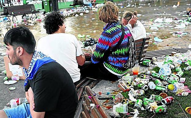 Un grupo de personas rodeado de residuos en un banco de El Arenal bilbaíno tras una noche de fiestas.