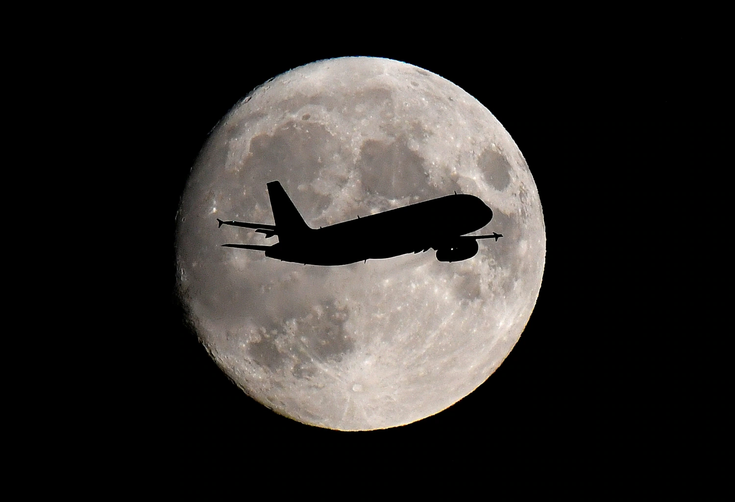 Un avión de pasajeros pasa frente a la luna mientras realiza su aproximación de aterrizaje final al aeropuerto de Heathrow en Londres, Gran Bretaña